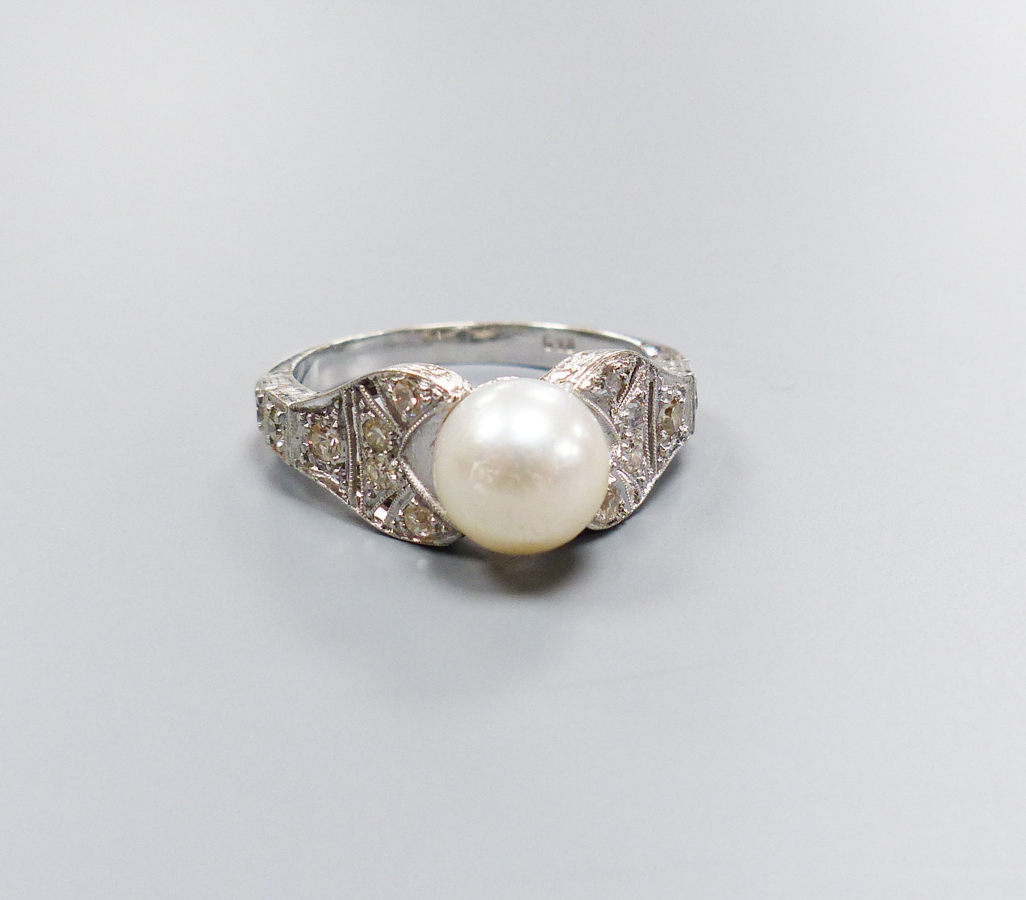 A modern 750 white metal and single stone cultured pearl dress ring, with diamond chip set pierced shoulders, size R/S, gross weight 5.5 grams.